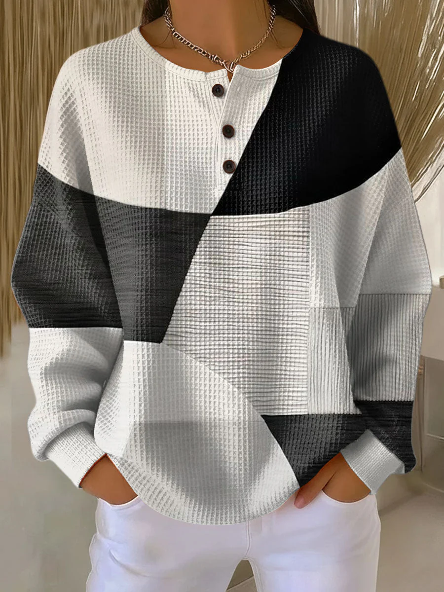 Elegancki i wygodny sweter kaszmirowy z nieregularnym wzorem w blokach kolorystycznych w kolorze czarnym, białym i szarym oraz półotwartym dekoltem.